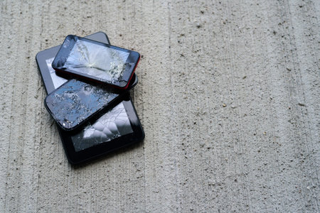 Broken phones and tablet on concrete background. Cracked screen