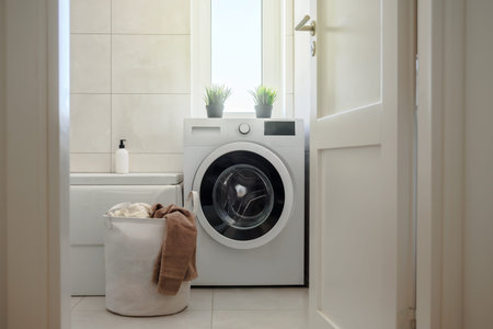 Washing machine in modern light bright bathroom. Laundry bag with towels near it. Scandinavian hygge...