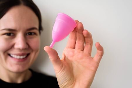 Yound Smiling Woman with pink menstrual cup in hand on grey background. Zero waste, reusable, eco conceptの写真素材