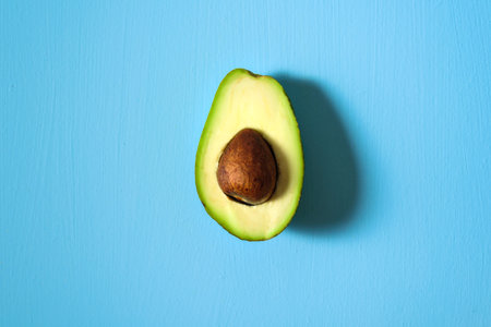 Avocado half on light blue background. Central conposition, hard light