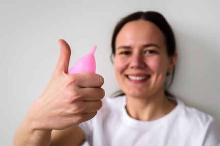 Yound Smiling Woman with pink menstrual cup in hand on grey background. Zero waste, reusable, eco conceptの写真素材