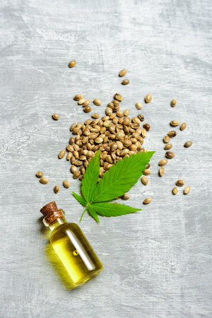 Hemp oil in glass bottle, seeds and leaf on grey concrete backgroundの写真素材