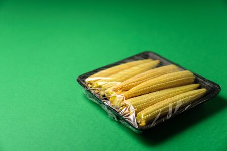 Fresh baby corn in plastic package. Zero waste, recycle concept. Plastic pollution. Green backgroundの写真素材