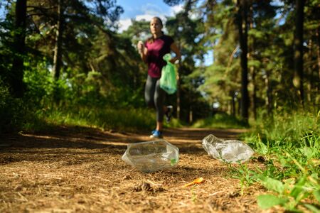 Woman jogging with garbage bag in forest. Collecting trash. Plogging conceptの写真素材