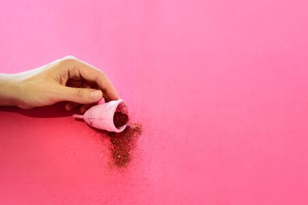 Menstrual cup full of red glitter in woman hand on pink background. Periods, eco alternative, reusable replacementの写真素材