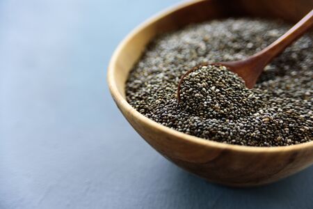 Chia seeds in old wooden bowl with wooden spoon on blue backgroundの写真素材