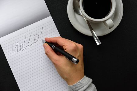 Bad handwriting with right hand. Word HELLO in note pad, pen and black coffeeの写真素材