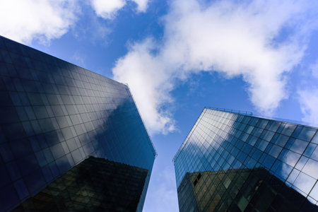 Two skyscrapers made from glass from below with blue sky and white beautiful cloudsの写真素材