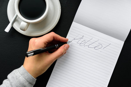 Bad handwriting with left hand. Word HELLO in note pad, pen and black coffee