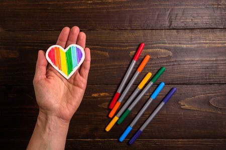 Handmade Valentines postcard with rainbow heart in woman hand on wooden backgroundの写真素材