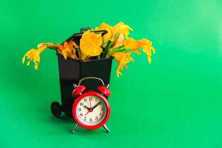 Black Dumpster with wilted narcissus flowers bouquet and red old style clock. Dead, aging concept....