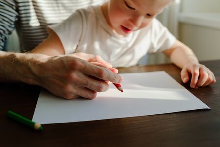 Father teaching child to write or draw with his hands. Red pencil and paper on wooden table. Homeschoolingの写真素材