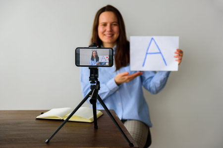 Woman teacher in shirt Recording video lesson at home for homeschooling children. Using smartphone