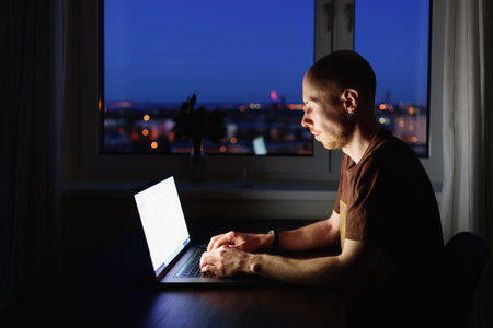Man working on laptop from home at night. Blue screen light