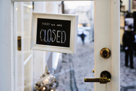 Sign CLOSED on restaurant or shop glass door. Street on background