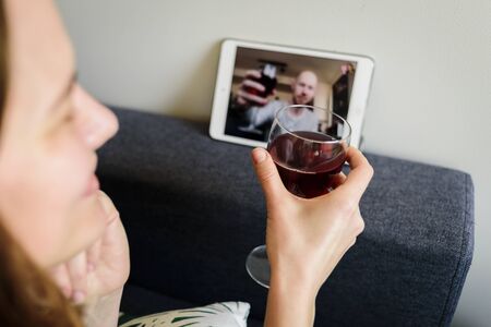 Woman drinking red wine online with male friend using tablet pc at homeの写真素材