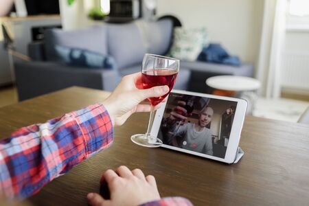 Woman drinking red wine online with male friend using tablet pc at homeの写真素材