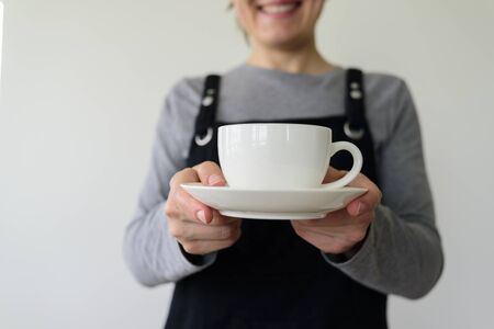 Woman waitress with cup smiling on gray background. Local businessの写真素材