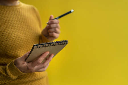 Woman Writing by left hand in notepad. Left hander day concept. In yellow sweaterの写真素材