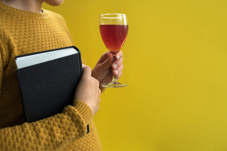Woman in yellow sweater holding book and glass of wine