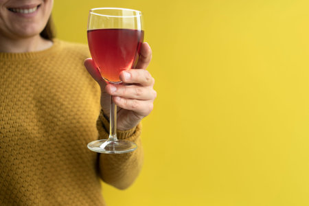 Woman in yellow sweater holding glass of wine in hand