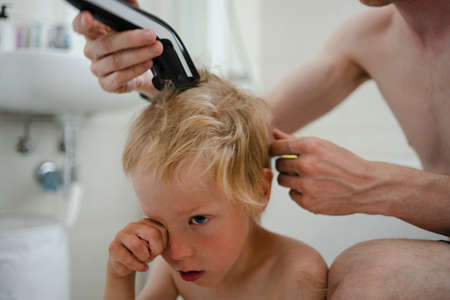 Father making haircut for son at home with haircut machine in bathroomの写真素材