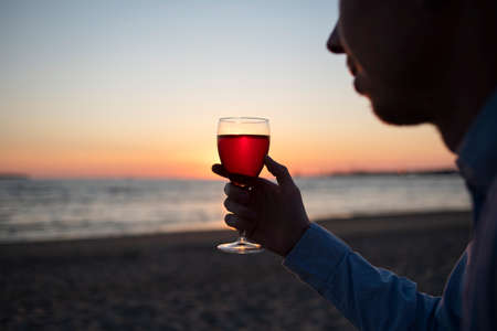 Man in shirt with glass of wine on beach at sunset. Enjoy life, slow livingの写真素材