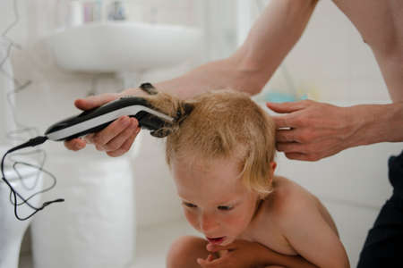 Father making haircut for son at home with haircut machine in bathroomの写真素材