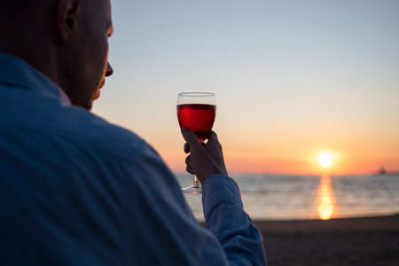 Man in shirt with glass of wine on beach at sunset. Enjoy life, slow livingの写真素材