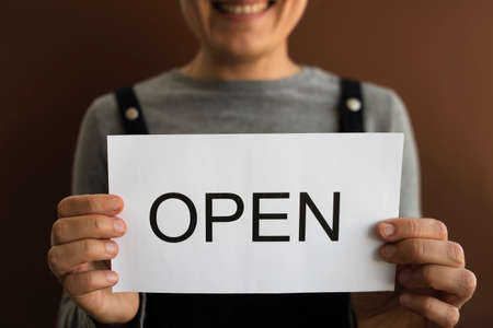 Woman with OPEN sign on brown background. Local business reopeningの写真素材