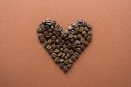 Heart-shaped coffee beans on brown background close up, flat lay