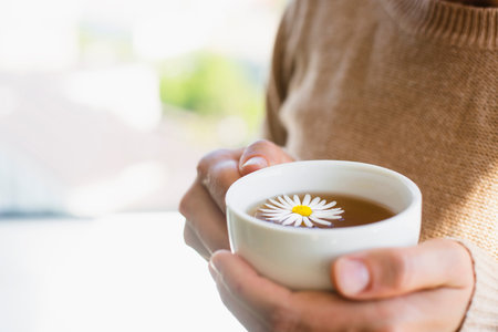 Cup of calming chamomile tea in woman hands in knitted sweater . Warm sunny autumn day