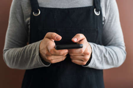 Woman in black apron using smartphone on brownの写真素材