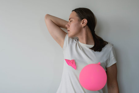 Woman with pink balloons on her breasts. Breast Cancer awareness month concept. One balloon burst,...