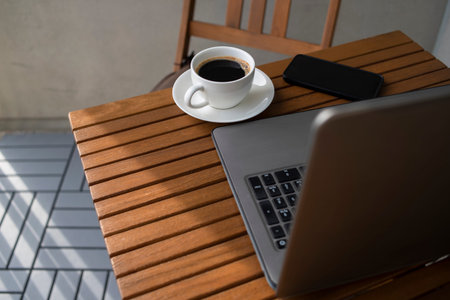 Still life for working in street cafe with laptop. Cup of coffee on wooden table.