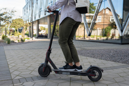 Woman riding at work on electric kick scooter near office building