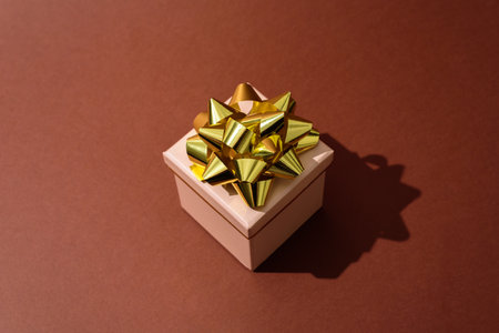 Beige Gift box with golden bow on brown background. Hard lightの写真素材