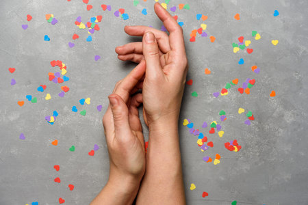 Hands with rainbow LGBT coloured hearts on concrete gray background
