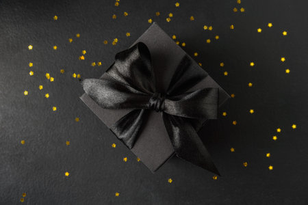 Black gift box with black bow and golden stars confetti. Top viewの写真素材