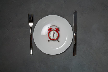 Plate with red alarm clock. intermittent fasting diet concept