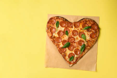 Heart shaped pizza pepperoni on yellow backgroundの写真素材