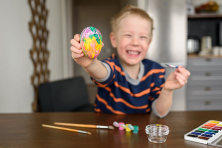 Happy smiling Boy coloring Easter egg at home with acrylic paint. Little artist, hobby