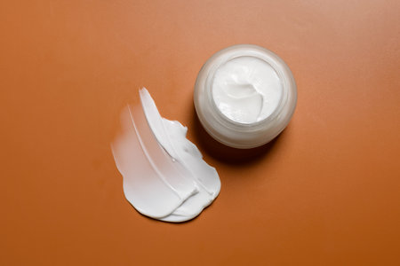 Glass skin cream jar on brown background with smear or swatch