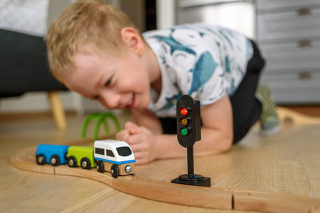 Little boy playing with wooden railroad at home. Smiling, happy face.
