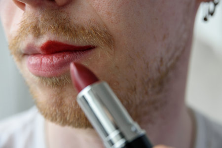 Bearded man applying red lipstick on his lipsの写真素材