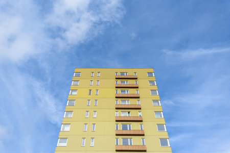 Tall green residential building against blue sky with clouds
