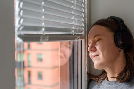 Woman in headphones listening to music near window and dreamingの写真素材