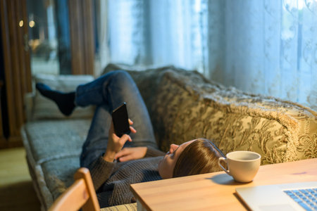 Woman using her phone laying on couch or sofa at home living room