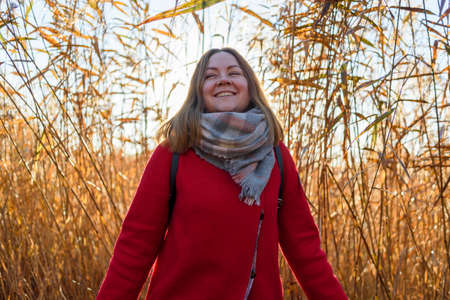 Happy smiling woman in red coat in reeds at sunriseの写真素材