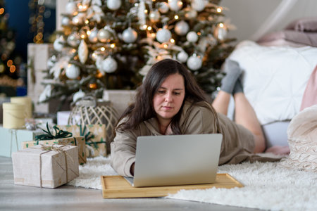 Woman using laptop in living room with Christmas decorations. Buying gifts, working from homeの写真素材